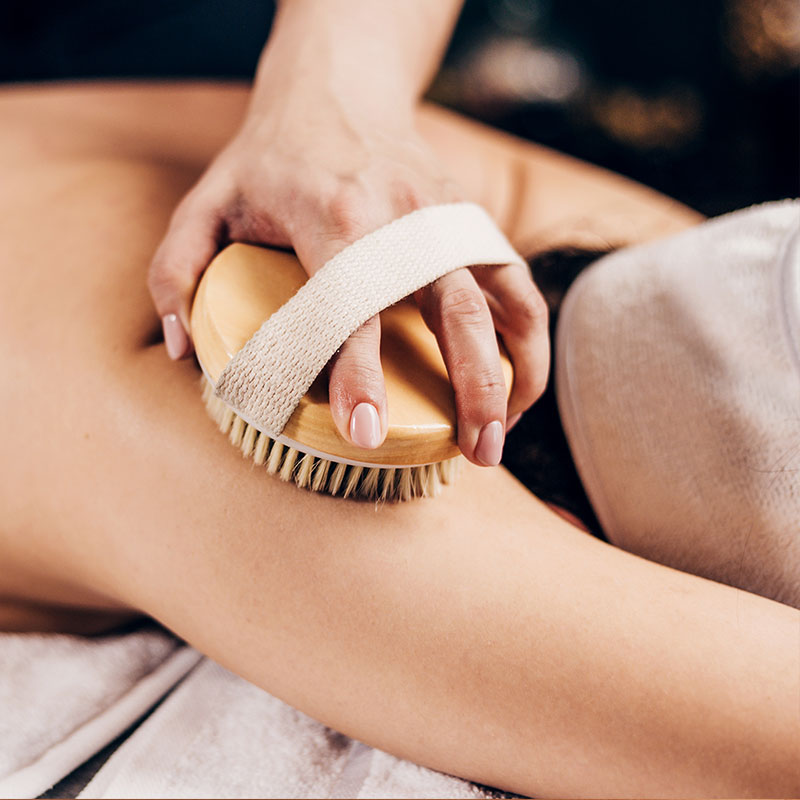 Trockenbürsten-Ganzkörpermassage mit Kupferborsten am Arm einer Kundin, zur Anregung der Durchblutung.
