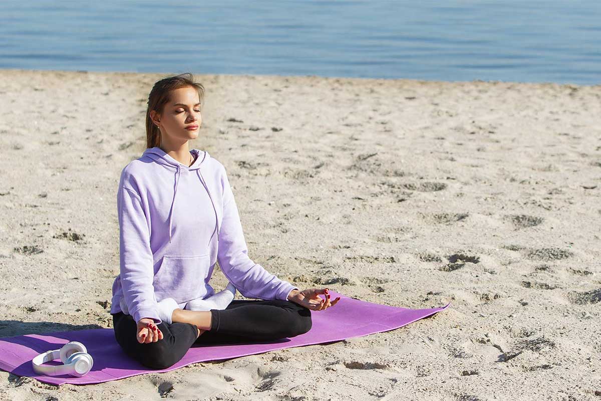 Eine Frau meditiert auf einer Matte vor dem Meer beim Yoga am Strand des Grand Hotel Binz auf Rügen.