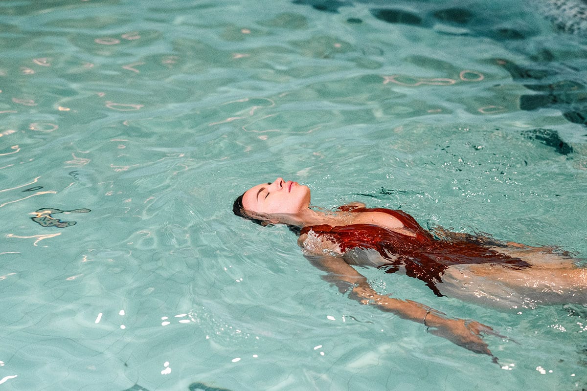 Woman in red swimsuit floating relaxed in pool, water softly reflecting the light